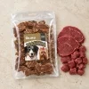 Flat-lay Masíčka 204901 (režim Produkt + suroviny): plný 300g sáček dle e-shop packshotu b64f08ae, syrové hovězí asymetricky, travertin, evergreen. Reference surovin AI-generovaná (HF job 8e2a8f68, 2,75 cr).