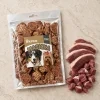 Flat-lay Masíčka 204863 (režim Produkt + suroviny): plný 300g sáček dle e-shop packshotu 1f2a6243, syrové kachní maso asymetricky, travertin, evergreen. Reference surovin AI-generovaná (HF job 20cf295c, 2,75 cr).