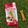 Flat-lay shora na trávě: sáček Žvýkadlo s buvolí kostí 12 cm (204049) a vedle volně ležící kost.