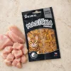 Flat-lay Masíčka Premium Hairball Control 50g (kočky) — produkt + syrové kuřecí maso na travertinu, evergreen kuchyňský mood.
