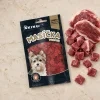 Úprava flat-lay (parent ed43c321): odstraněna dýně, vedle sáčku pouze syrové kachní maso. Travertin, top-down.